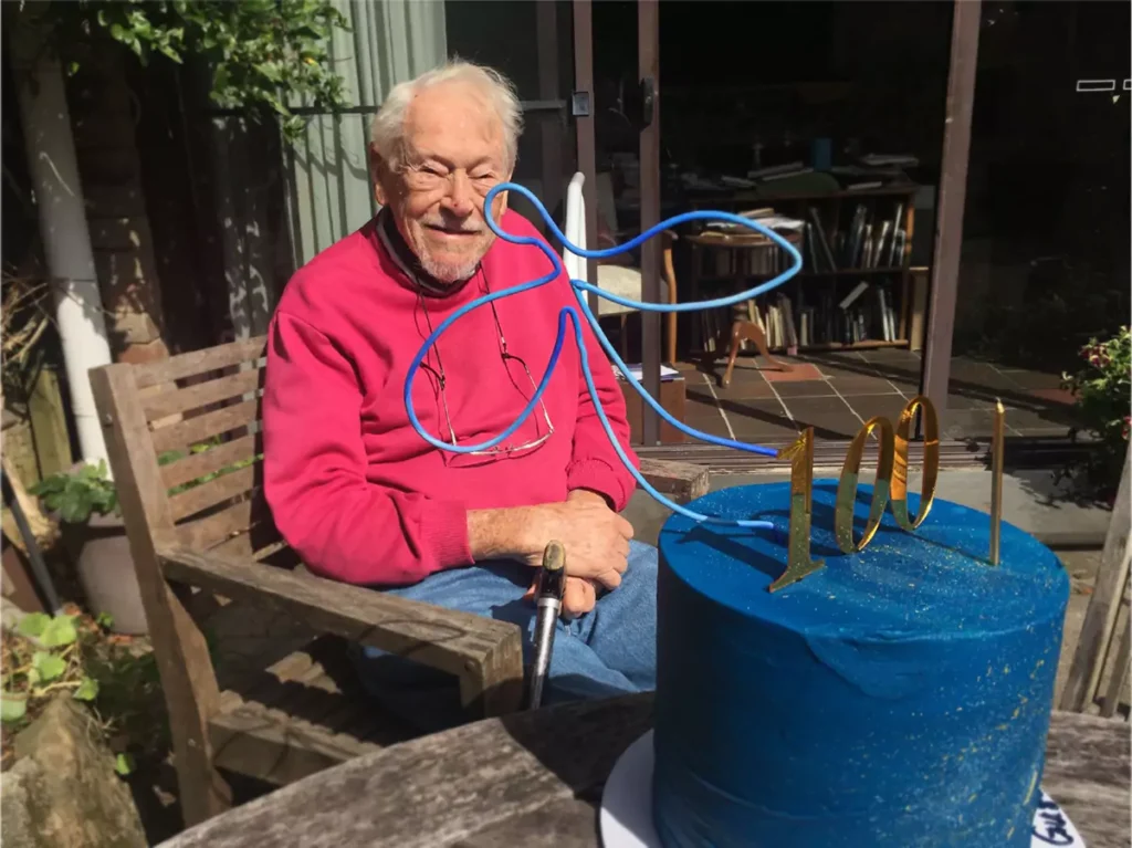 Happy elderly man sitting in front of cake with the number 100 on top
